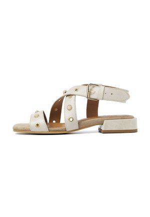 Hvide læderhælede sandaler med udskæringsdesign, guldfarvet hardware og en lav blokhæl. Justerbar ankelrem for bedre pasform.