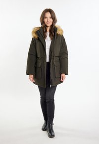 Olijfgroene parka met een nepbont capuchon, twee voorzakken, een ritssluiting en verstelbare koorden in de taille. Zwarte jeans en laarzen.