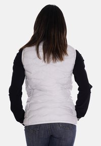 Gilet en duvet blanc avec un design matelassé, porté par-dessus une chemise à manches longues noire. Texture lisse, coupe ajustée, détails de couture visibles.