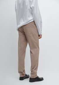 Jasnobrązowe spodnie o prostym kroju wykonane z bawełny, z dwiema tylnymi kieszeniami i subtelnymi detalami w stębnówce. W połączeniu z białą, w paski koszulą.