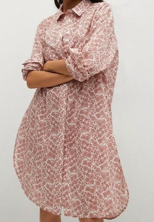 Robe-chemise boutonnée en tissu doux et léger, arborant un motif floral rouge sur fond crème, avec des manches retroussées et une coupe décontractée.