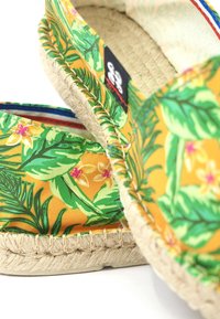 Espadrilles jaunes avec motif de feuilles vertes et de fleurs. Dessus en tissu, semelle en jute tressé et garniture en tissu coloré.