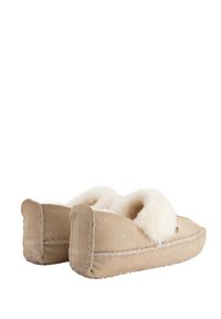 Beige suède slippers met een zachte, witte bontvoering. Kenmerken zijn de zichtbare stiksels en de afgeronde vorm. Slip-on ontwerp zonder sluitingen.