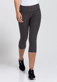 Leggings capri gris en tissu extensible avec une large ceinture, offrant une texture lisse et une silhouette ajustée. Des chaussures de sport noires complètent la tenue.