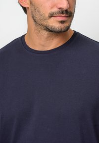 Mörkblå bomulls t-shirt med rund halsringning, slät yta och korta ärmar, visad på en person från bröstet och upp.