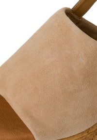 Sandalo con zeppa in suede beige, caratterizzato da una ampia fascia superiore e una parte inferiore in pelle marrone, con una suola in sughero texturizzato.