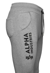 Graue Baumwoll-Sweatpants mit Seitentaschen, versehen mit einem schwarzen "ALPHA INDUSTRIES" Logo, das entlang des linken Beins aufgedruckt ist, und einem verstellbaren Kordelzugbund.