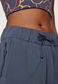 Inimese keskosa lähivõte, kes kannab tumel siniseid elastse vöökohaga pükse, millel on pael, ja mustrilist lühikest topi.