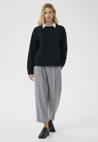 Dark navy knitted sweater with a round neckline, paired with gray pinstriped wide-leg trousers and black slip-on shoes.