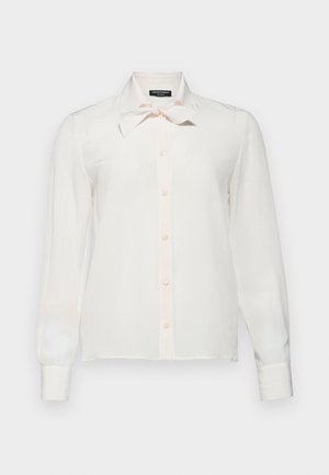 Chemisier blanc à manches longues avec un col à nœud et un devant à boutons. Texture lisse, tissu doux et coupe slim avec des accents rose pâle.