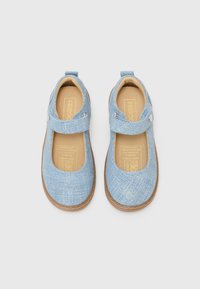 Chaussures Mary Jane en tissu bleu avec une surface texturée, une sangle sur le pied et une semelle en caoutchouc marron. Coutures discrètes le long du bord.
