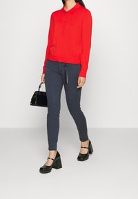 Czerwona długosleeve'owa polo sweter z kołnierzykiem i guzikami, w połączeniu z ciemnoniebieskimi slim fit spodniami. Czarne lakierowane buty na słupku i torebka.