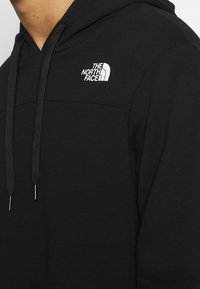 Black hoodie with a soft texture, featuring a front kangaroo pocket, adjustable drawstrings, and a small white logo on the upper left chest.
