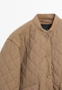 Veste matelassée marron clair avec col rond et trois boutons assortis sur le devant, présentant un motif de couture en forme de losange.