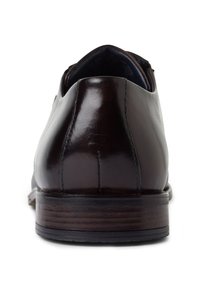 Chaussure habillée en cuir marron avec une surface lisse et brillante, un talon arrondi et des accents cousus le long du dos pour plus de détail.