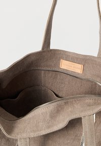 Τσάντα tote από μπεζ ύφασμα με δύο ανθεκτικούς ιμάντες, με υφή στο εσωτερικό και δερμάτινη ετικέτα που αναγράφει «Vanessa Bruno, Κατασκευασμένο στη Γαλλία».