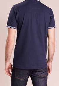 Polo shirt bleu marine avec un col à rayures blanches, manches courtes et ourlet droit. Fabriqué en coton avec une texture lisse et un design minimaliste.