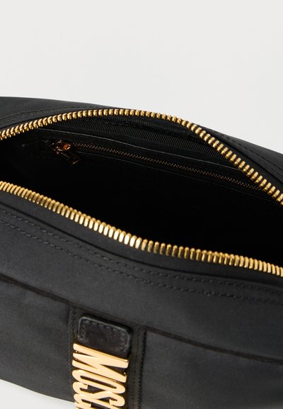 Μαύρη υφασμάτινη τσάντα με χρυστό φερμουάρ και μεταλλικά στοιχεία. Διαθέτει απαλό ύφασμα και λογότυπο. Το εσωτερικό έχει φόδρα και είναι σκούρου χρώματος.