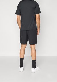 Czarna sportowa koszulka i spodenki z lekkiego materiału. Założone z czarnymi skarpetami i białymi trampkami, widziane od tyłu.