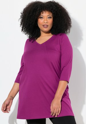 Purple tunic top with a V-neckline and three-quarter sleeves, made from soft fabric with a loose, relaxed fit. Features side seam detailing.