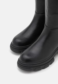 Black rubber boots with a smooth finish, rounded toe, and thick textured soles. Features a tall shaft and subtle seam detailing.