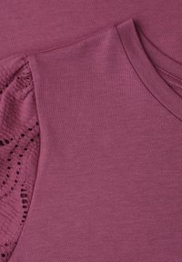 Gros plan d’un haut en tissu tricoté mauve avec manches courtes, présentant un détail complexe de dentelle ajourée et un col rond côtelé.
