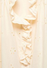 Blusa leggera color crema con scollo a increspature, caratterizzata da un motivo floreale ricamato e dettagli a intaglio su tutta la stoffa. Materiale morbido e leggero.