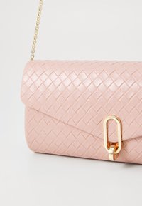 Gewebte rosa Leder-Handtasche mit abgerundetem Deckel, goldenen Beschlägen und einer Kettenriemen. Enthält ein rechteckiges goldfarbenes Schlaufen-Detail auf der Vorderseite.