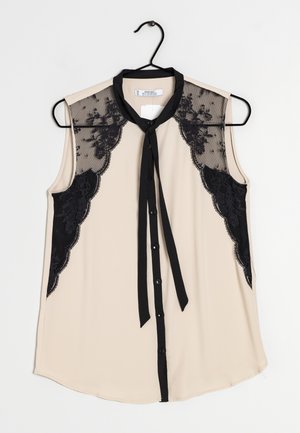 Blouse sans manches en beige avec des accents en dentelle noire sur les épaules et à l'avant, dotée d'une fermeture à cravate noire et d'un devant à boutons.