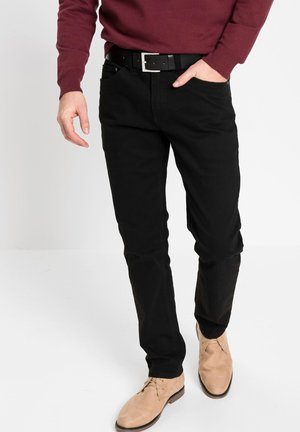 Schwarze Baumwollhosen mit schlankem Schnitt, klassischen Taschen und kombiniert mit einem schwarzen Gürtel und beigen Wildlederschuhen.