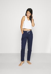 Navyblauwe joggers met een tunnelkoord in de taille en zijzakken, gecombineerd met een witte cropped tanktop met een gladde textuur.