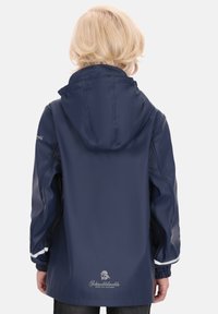 Vandeniui atspari tamsiai mėlyna striukė su gobtuvu, turinti elastinius rankogalius, baltas detales palei rankoves ir logotipą apatinėje nugaros dalyje. Lygus paviršius.