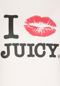 La maglietta bianca presenta il testo nero "I JUICY" e un'impronta di labbra rosse. Il font è audace e rotondo, con una texture lucida sulle labbra.