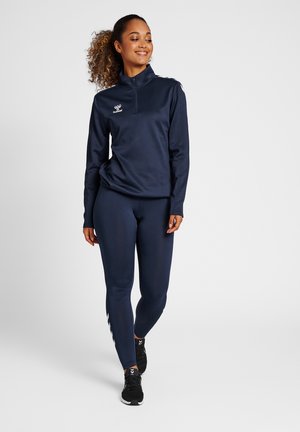 Marineblå atletisk pullover med lynlås krave og logo, parret med tætsiddende leggings, der har en glat tekstur og slankt design. Sorte løbesko.