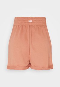 Růžové Nike šortky barvy broskve s gumičkovým pasem, ohrnutým lemem a měkkou bavlněnou tkaninou, která jemně texturuje.