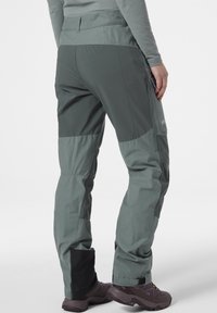 Technické outdoorové kalhoty v tmavě zelené barvě, vyrobené z lehkého materiálu. Mají zesílené panely, kapsu na zip a nastavitelné nohavice.