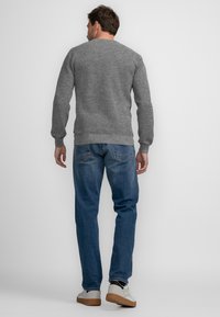 Grau gestrickter Pullover mit Rundhalsausschnitt, kombiniert mit blauen Jeans, getragen mit weißen Schuhen. Die Struktur ist grob und tailliert.