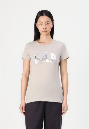 Beige cotton t-shirt with short sleeves, round neckline, and silver printed "GAP" logo. The fabric appears soft and smooth.