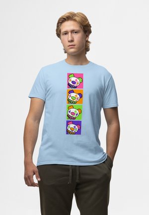 Jeune homme portant un t-shirt bleu clair avec quatre visages colorés de clowns dessin animé empilés verticalement sur le devant.