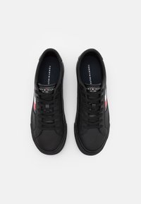 Zapatillas de cuero negro con suela plana, diseño de cordones y acentos en rojo y azul a los lados. Marca visible en la plantilla.