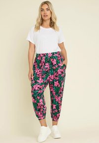 Flerfärgade blommiga byxor med rosa blommor på grön bakgrund, elastisk midja och sidofickor, kombinerat med en enkel vit t-shirt.