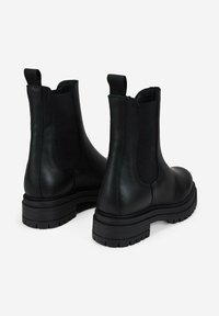 Botas Chelsea de cuero negro con paneles laterales elásticos y una suela gruesa con un dibujo en el tacón. Acabado liso; con tiradores en la parte trasera.