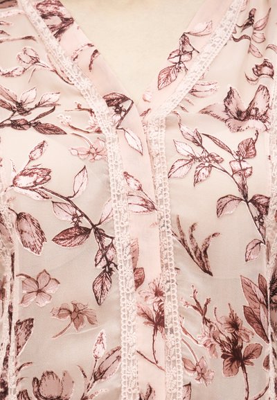 Tissu léger rose pâle transparent avec des motifs floraux détaillés rose foncé et une bordure en dentelle verticale le long d'un décolleté en forme de V.