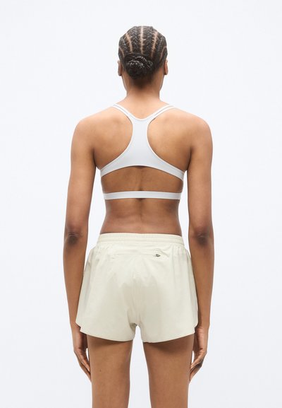 Ανοιχτό γκρι αθλητικό σουτιέν με σχέδιο racerback και ρυθμιζόμενους ιμάντες, συνδυασμένο με μπεζ αθλητικές βερμούδες με ελαστική μέση.