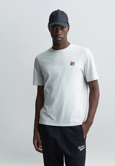 T-shirt in cotone grigio con maniche corte, caratterizzato da un piccolo design di tigre ricamato arancione sul petto. Indossato con pantaloni della tuta neri.