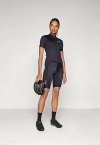 Čierny cyklistický dres s krátkymi rukávmi, doplnený o čierne šortky s polstrovaním. Obsahuje čiernu prilbu a cyklistické topánky, na neutrálnom pozadí.