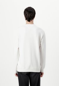 Hvid sweatshirt med lange ærmer, ribbede manchetter og kant, med V-formet sømdetalje på bagsiden. Bæres med mørke jeans.