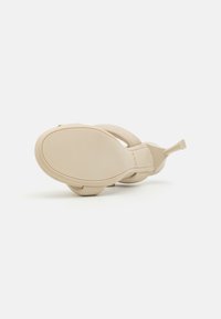 Beige sandaler med en glatt, matt finish, med et åpen tå-design, rund såle og en subtil hengseldetalj ved hælen.