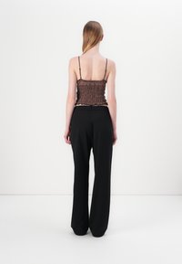 Smeđi krojeni crop top s tankim naramenicama, uparen s visokim crnim širokim hlačama. Glatka tkanina s opuštenim krojem.