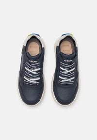 Sneaker in pelle blu navy con lacci bianchi, suole color crema e un accento blu sul tallone. Presentano perforazioni per la traspirabilità.